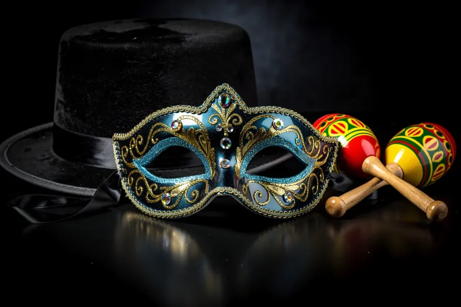 Un masque de bal chatoyant bleu et or repose sur une surface noire, accompagné d’un chapeau de magicien et de maracas.